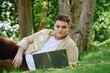 © Bliss - A queer person relaxes in a lush green setting while using a laptop, embracing natures tranquility.