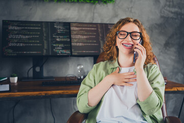 Photo of young hacker programmer girl speak phone laugh wear shirt workstation loft office indoors