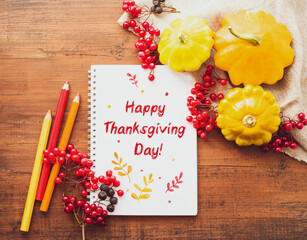 Wall Mural - Happy Thanksgiving Day! White notebook with colored pencils, yellow squash with red viburnum berries on old wooden surface, top view.