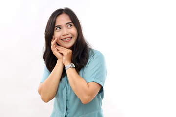 Indoor shot of cheerful woman keeps hands together smiles toothily concentrated away with glad expression feels very glad wears casual shirt poses against white background blank space