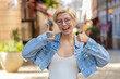 © Andrii Iemelianenko - Like. Happy woman shows thumbs up agrees with something or gives positive reply recommends advertisement likes good idea feedback, celebrating success victory. Blonde girl on urban city street.