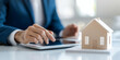 © Jaruwan photo - real estate agent using tablet to showcase property listings with model house on table, demonstrating professionalism and modern technology in real estate