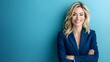 © michaswelt - A confident blonde businesswoman in a blue suit beams warmly against a clean blue background, highlighting her professional image.