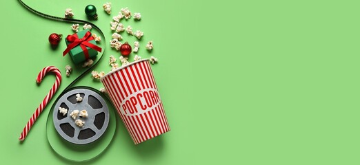 Canvas Print - Bucket of popcorn, film reel, gift box and decorations on green background with space for text. Christmas movie concept