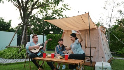 Family together camping. Father play guitar, mother and daughter selfie. Parent use outdoor camping activity to communicate and spending time with young generation cross generation gap. Divergence.