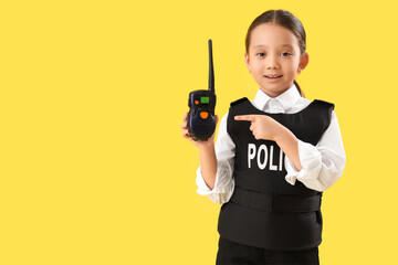 Cute little police officer pointing at radio transmitter on yellow background. Opposite Day celebration