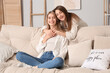 © Pixel-Shot - Young woman hugging her friend on sofa at home