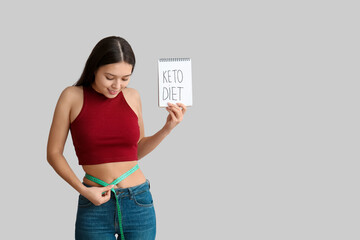 Poster - Beautiful young happy Asian woman holding notebook with text KETO DIET and measuring tape on grey background