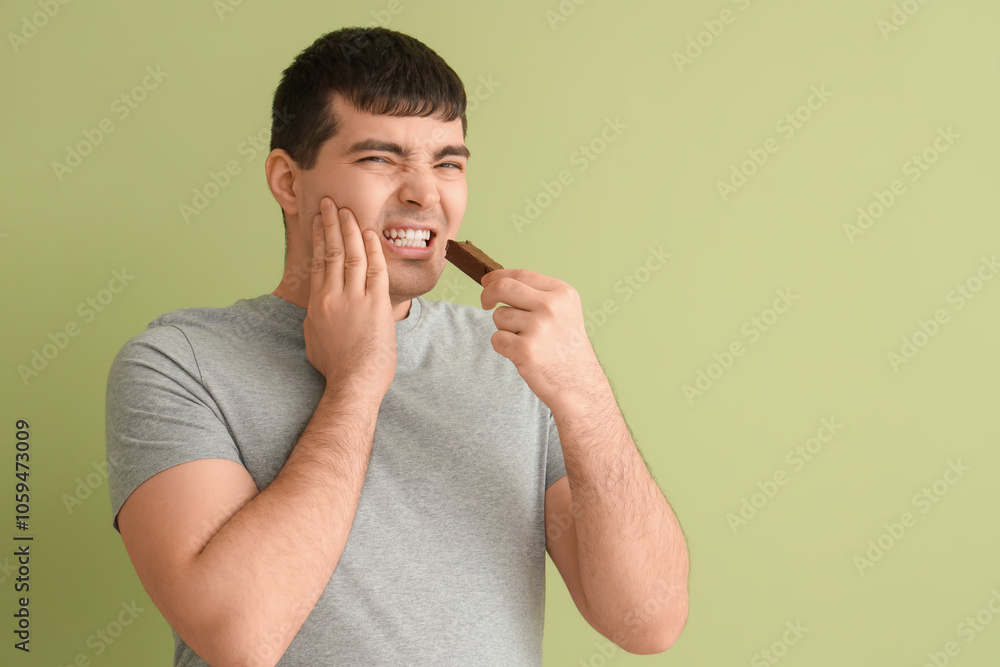 Young man with candy bar suffering from toothache on green background