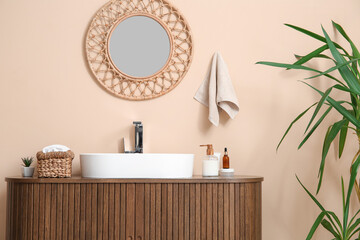 Modern sink and bath supplies on wooden chest of drawers near beige wall in bathroom