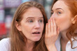 © Iryna - Two women share secrets outdoors in a vibrant urban setting during daylight in an intimate moment of connection