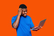 © Iryna - A young man in a blue shirt smiles with surprise while using a laptop against an orange background
