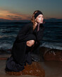 © Tanya Danilevich/Stocksy - The girl sitting on the stone on the beach at sunset.
