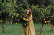 © Adrian Cotiga/Stocksy - Lady in green dress happily harvesting oranges in garden.