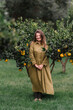 © Adrian Cotiga/Stocksy - Smiling lady in green dress among orange trees in orchard.
