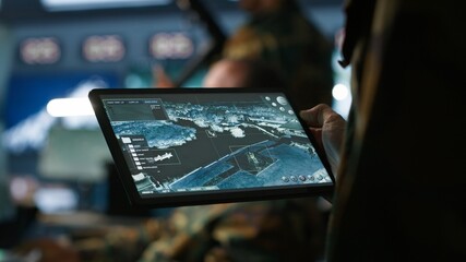 Military agent working in control room, using software on tablet, analyzing aerial reconnaissance data. Close up of intelligence corps expert controlling drones with portable device, camera A
