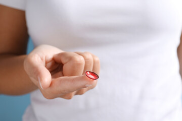 Woman holding color contact lens on light blue background, closeup