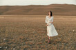 © SHOTPRIME STUDIO - Woman standing in white dress in open field with mountains in background, serene travel beauty in nature scene