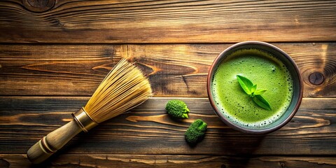 A bowl of frothy green tea with a sprig of fresh leaves, a bamboo whisk, and two small leafy sprigs on a wooden surface.