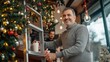 © Daria Lukoiko - A middle-aged Smiling caucasian man cafe owner stands on a ladder, hanging Christmas lights around the large front window of the coffee shop. he decorates with festive garlands a holiday atmosphere