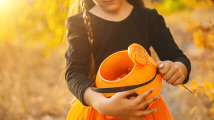 Close-up portrait of a 4-5 year old girl in a witch costume with a candy bucket against a background of autumn leaves. Copy space.