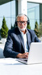 © Rysak - man a blue suit uses a laptop outdoors