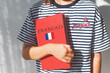 © Evgeniia Primavera - one white girl child schoolgirl with t-shirt with i love you in french and french textbook with french inscription and flag of France, foreign language learning concept