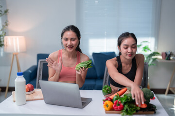 two asian sportswomen greeting on a video call and preparing healthy food, discussing nutrition and 