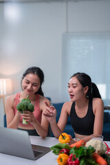 Two asian nutritionists having video conference with client on laptop, discussing healthy eating and showing fresh vegetables, promoting balanced diet and online nutrition consultation