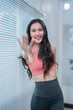 © Tj - Young asian fitness woman wearing sportswear, waving hand and smiling while standing by window blinds in gym, representing healthy lifestyle and wellness