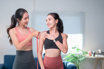 Personal trainer is measuring her client's shoulder circumference with a tape measure, tracking progress and ensuring proper fitness assessment during a home workout session