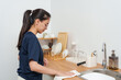 © Ekkasit A Siam - Young Asian woman drying kitchen countertop with cloth in neat, organized kitchen space, showing relaxed and focused expression, embodying calm, mindful homekeeping during personal time.