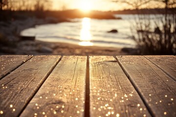 A close-up of a wooden table at the edge of a body of water with the sun setting in the background.