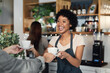 © peopleimages.com - Waitress, happy and customer with coffee order in cafe for breakfast, retail sale and hospitality service. Small business, barista and serving latte beverage by counter in bistro for caffeine drink