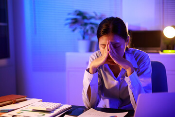 Asian woman diligently works overtime, managing a heavy workload with focus and determination. Despite the challenges, her commitment shines through as she strives  and meets her deadlines.