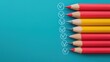 © Nitchalee N. - A row of colored pencils in red and yellow rests on a teal background, accompanied by checkmarks, suggesting an organized or creative task.