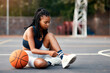© peopleimages.com - Black woman, basketball and tying shoes at court for exercise, training and beginning of game. Player, fitness and athlete with footwear on ground for sports competition, start or match preparation