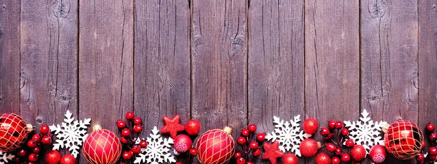 Aufkleber - Christmas bottom border of red  baubles, snowflakes and berries. Top down view on a dark wood background. Copy space.