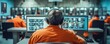 © I Have Photos - A person wearing orange jumpsuit sits at a computer monitoring security cameras.