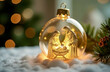 © Lelya - Close-up of a Christmas ornament in the form of a glass sphere with a gold-colored interior, the ornament illuminates the figures of Joseph, Mary and baby Jesus carved in glass. Nativity scene