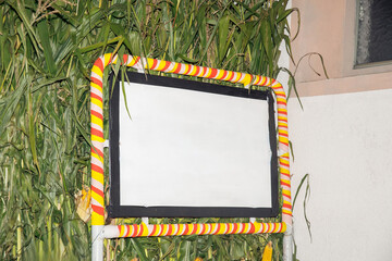 Blank billboard with yellow and red striped frame against overgrown greenery background