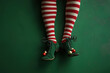 © Klay - christmas elf legs in striped red and white stockings with green shoes and holiday decorations on a green background