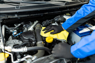 Wall Mural - A mechanic performing maintenance on a car engine using a cleaning cloth in an automotive repair shop during the afternoon