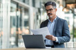 © Impressionstock - Focused Businessman Analyzing Documents Reviewing Important Papers with Laptop in Modern Office