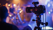 © Enigma - Professional video camera recording a live music concert on stage with blurred musicians in the background under colorful lights