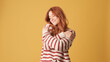 © Andrii Nekrasov - Cute red-haired woman dressed in sweater hugs herself looking at camera on yellow background. Beautiful girl poses in studio with blank space on yellow wall for your promotion