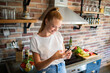 © Geber86 - Young woman holding smartphone in modern kitchen