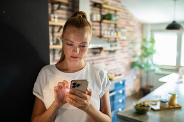 Wall Mural - Young woman holding smartphone in modern kitchen