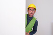 © KrishnaTedjo - Asian civil engineer peeking from behind a wall showing shocked face expression