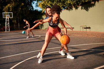 Wall Mural - Bounce, basketball and women playing game together for competition, challenge and fitness on playground. Outdoor, sports and girl friends on court with ball, exercise and teamwork at community club